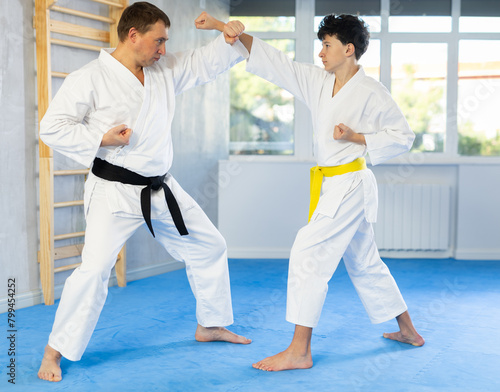 Sportive teenage boy applying blocking and kicking techniques on middle-aged trainer during karate classes © JackF