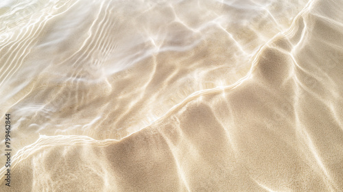 Close-up image capturing the peaceful interaction between clear, shallow waters and the soft sands of a tranquil beach, creating delicate ripples and patterns in the sunlight