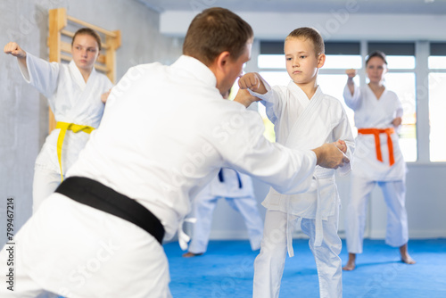 Boy train and learn during family group lesson in oriental martial arts. Man teacher corrects pose posture position of body, hands during karate classes.