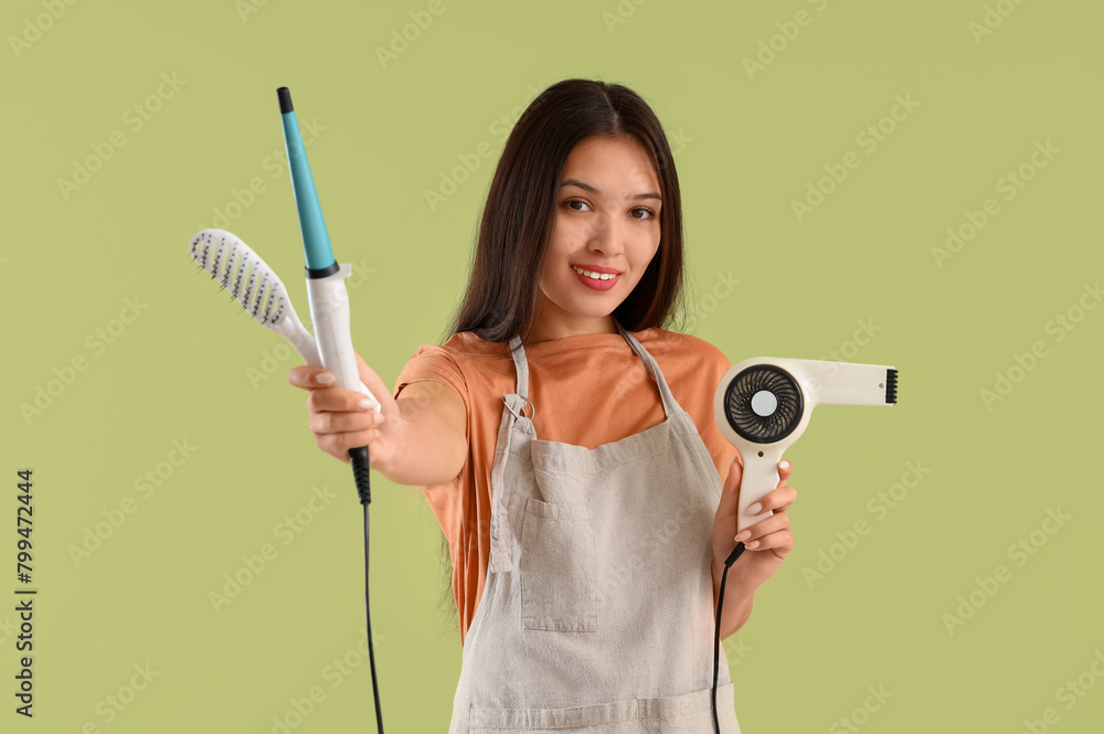 Beautiful Asian happy female hairdresser with hairdryer, curling iron and brush on green background Beautiful Asian happy female hairdresser with hairdryer, curling iron and brush on green background