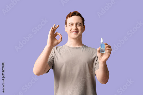 Young man with sanitizer showing OK on lilac background