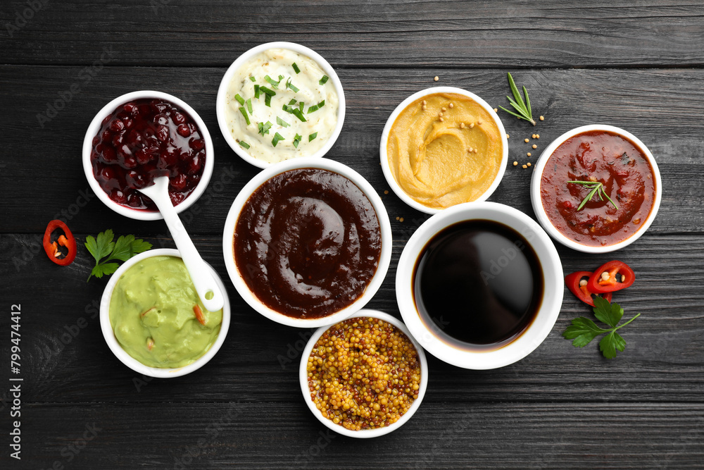 Different tasty sauces in bowls, parsley, chili pepper and rosemary on black wooden table, flat lay Different tasty sauces in bowls, parsley, chili pepper and rosemary on black wooden table, flat lay