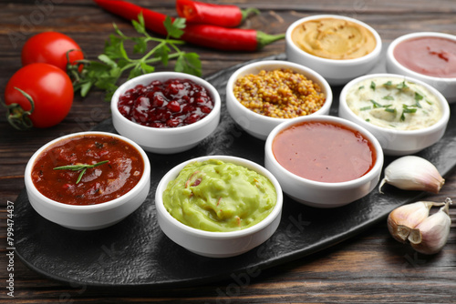 Different tasty sauces in bowls and ingredients on wooden table, closeup