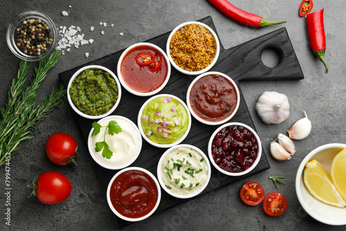 Different tasty sauces in bowls and ingredients on grey table, flat lay