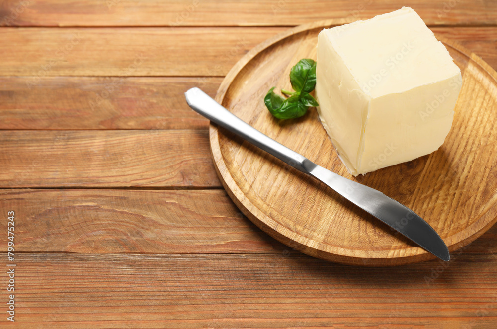 Block of tasty butter, knife and basil on wooden table. Space for text