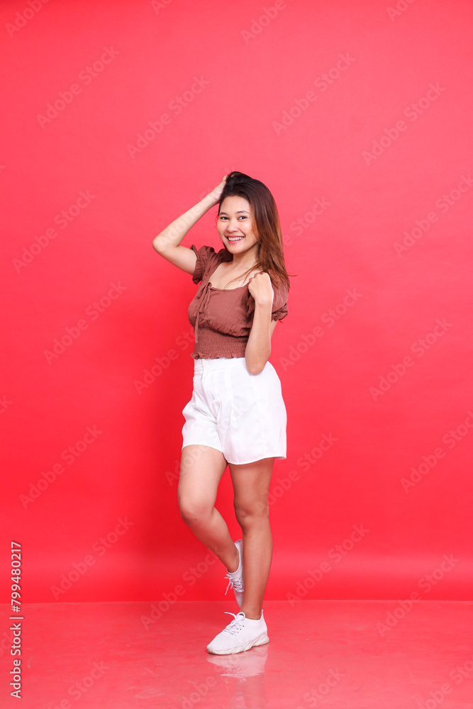 the charm of a cheerful Asian woman holding her shoulders and head wearing a brown blouse and shorts on a red background. for fashion, lifestyle and clothing concepts the charm of a cheerful Asian woman holding her shoulders and head wearing a brown blouse and shorts on a red background. for fashion, lifestyle and clothing concepts