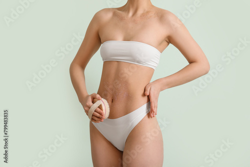 Young woman with massage brush scrubbing stomach on light background