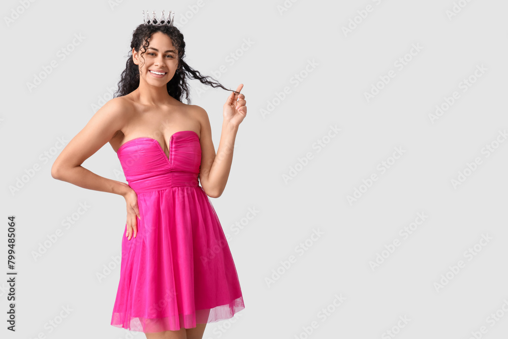 Happy young African-American woman in stylish pink prom dress and tiara on grey background Happy young African-American woman in stylish pink prom dress and tiara on grey background