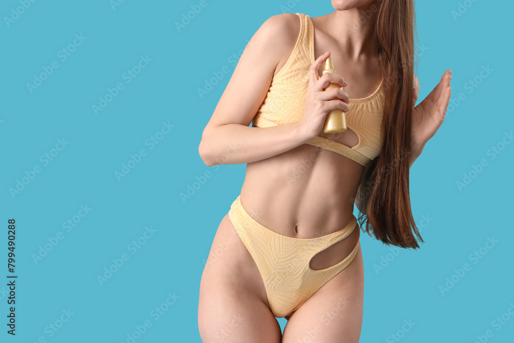 Naklejka premium Beautiful young woman in bikini with hair spray on blue background