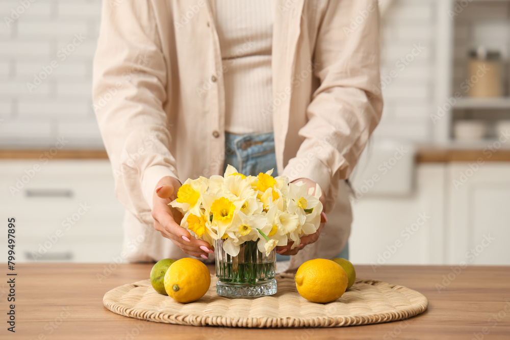 Obraz premium Young woman with bouquet of daffodils and fruits on table at home