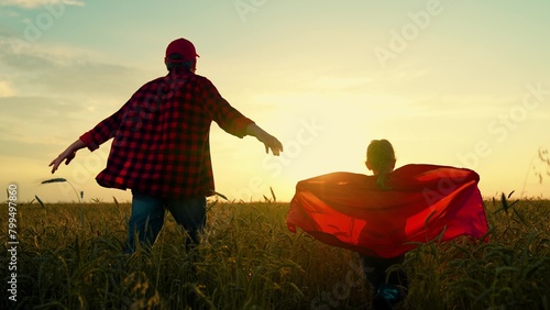 Dad, girl dreams of becoming superhero, fly in red cape. Dad of daughter plays superheroes in wheat field. Dad child run around in red raincoats, playing outdoors. Family carnival in field, Halloween