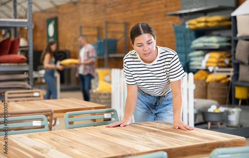 Girl buyer before buying furniture inspects table goods for defects and flaws. Customer in garden furniture store inspects countertop and imagine product in patio