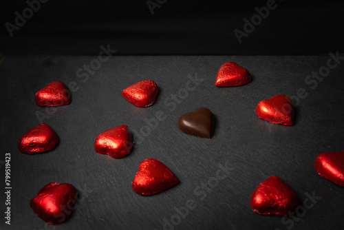 Group of heart shaped chocolates with red wrapper, one of them is without wrapper