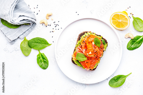 Avocado and salmon toast on rye bread with spinach, cashew and sesame seeds, white table background, top view