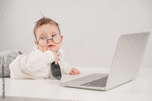 Cute baby in glasses and suit working on laptop. 