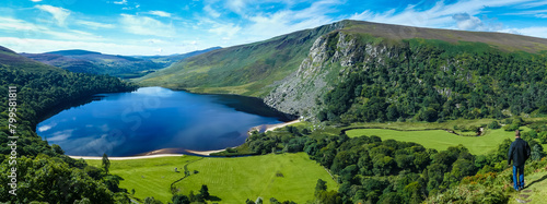 Panoramic shot of a calm lake surrounded by greenery-covered hills in Wicklow county town of Ireland