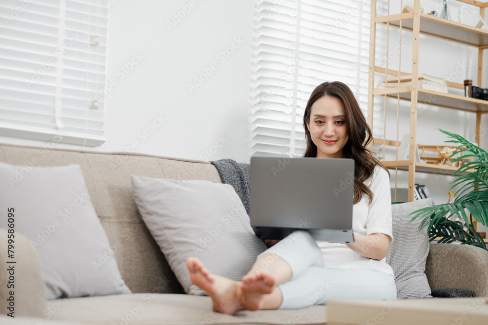 Relaxed woman enjoys working from home, comfortably lounging on a couch with her laptop in a well-lit living space. Relaxed woman enjoys working from home, comfortably lounging on a couch with her laptop in a well-lit living space.