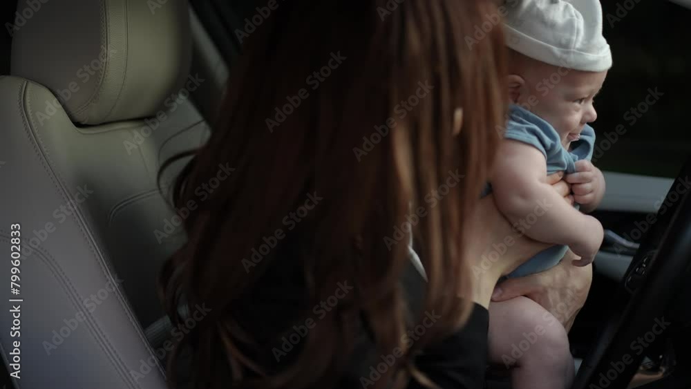 Close-up. A woman sits in the driver's seat of a car with a baby in her ...