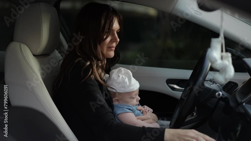 A woman sits in the driver's seat of a car with a baby in her arms and starts the engine in the car photo