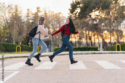 two student girls crossing crosswalk holding her hands, running and smiling