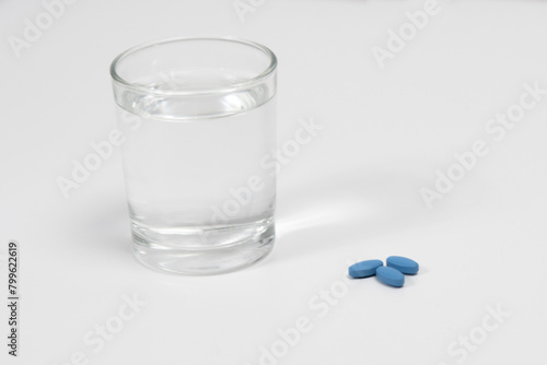 Blue pills for treating erectile dysfunction on a white table with glass of water
