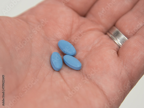 Blue pills for erectile dysfunction held in palm of hand.