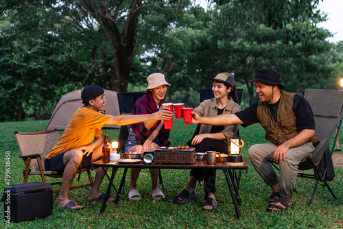 Happy asian diverse group friends enjoy drinking a beer together. They feeling relaxed and refreshing while camping in the nature at night. Recreation and journey outdoor activity lifestyle.