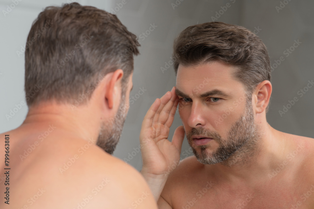 Obraz premium Close-up portrait of perfect brunet man touching chin and skin. Handsome man touching face in front of the mirror in bath. Perfect skin. Man cosmetic, skin treatment. Hygiene and skin care male face.