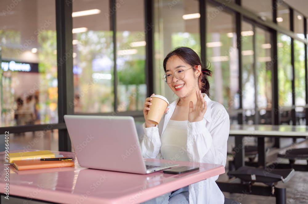 A female college student is having a meeting video call while sitting at a table in a cafeteria. A female college student is having a meeting video call while sitting at a table in a cafeteria.