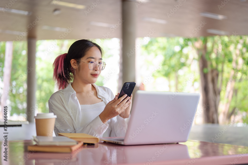 Obraz premium A female college student using her smartphone while sitting at a table in a campus cafeteria.