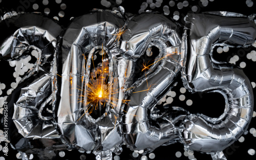 Happy new year 2025 metallic balloons with confetti and sparkler firework Bengal lights on dark black background. Greeting card silver foil balloons numbers Christmas holiday concept. Celebration