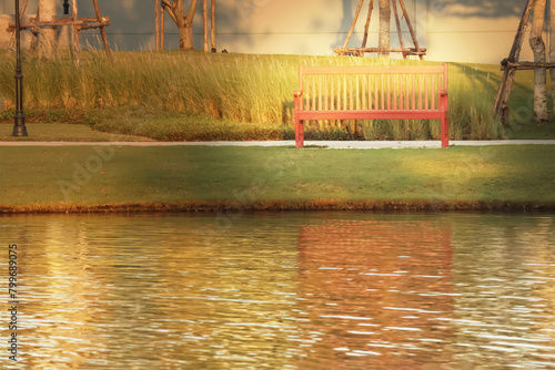 Wooden bench with bright sunlight in the park and reflection image on the peaceful lake imply sad and loneliness atmosphere.