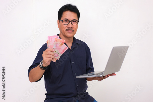 A middle-aged man holding some money in one hand and open laptop in the other photo