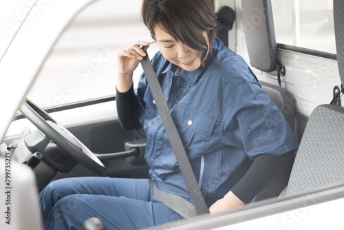 トラックを運転する中年の作業着の女性 運送や配送業などのイメージ シートベルトでご安全に