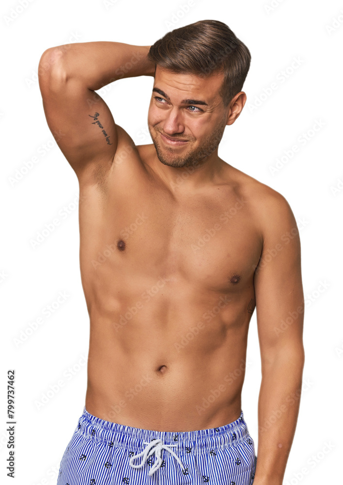Young man shirtless in swimwear, studio touching back of head, thinking and making a choice. Young man shirtless in swimwear, studio touching back of head, thinking and making a choice.