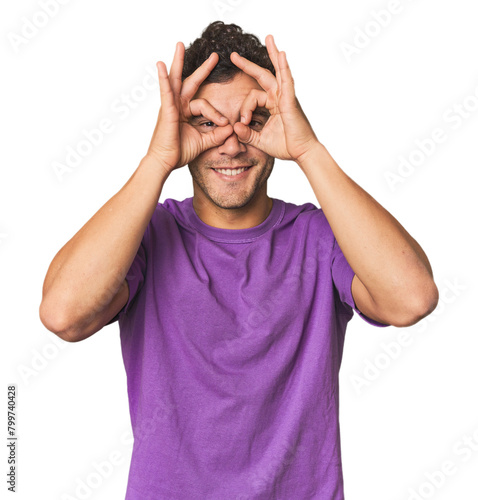 Young Hispanic man in studio showing okay sign over eyes