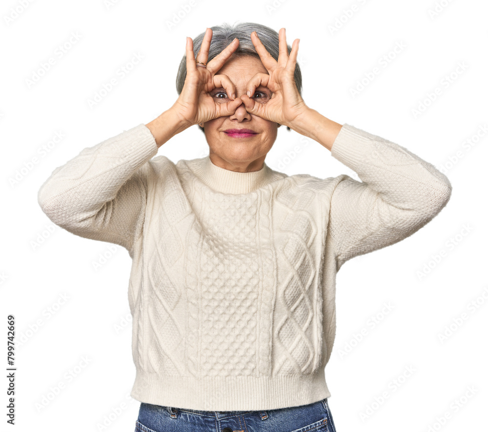 Caucasian mid-age female on studio background showing okay sign over eyes Caucasian mid-age female on studio background showing okay sign over eyes