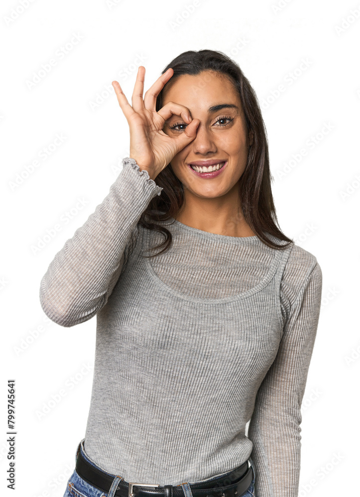 Hispanic young woman excited keeping ok gesture on eye. Hispanic young woman excited keeping ok gesture on eye.