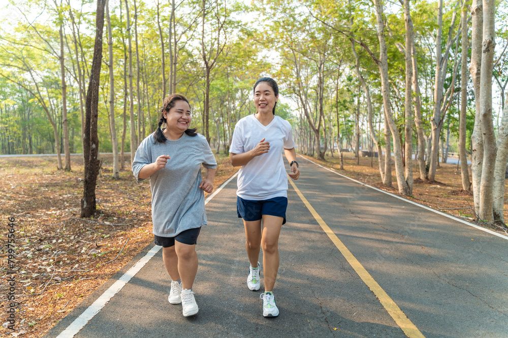 Two happy Asian female friends running together in the morning at a running park on a summer day