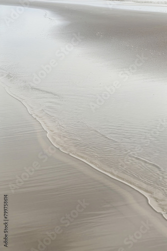 A minimalist beach scene featuring the linear patterns of receding tide lines in the sand  with their smooth curves and subtle variations in tone creating a serene and harmonious composition