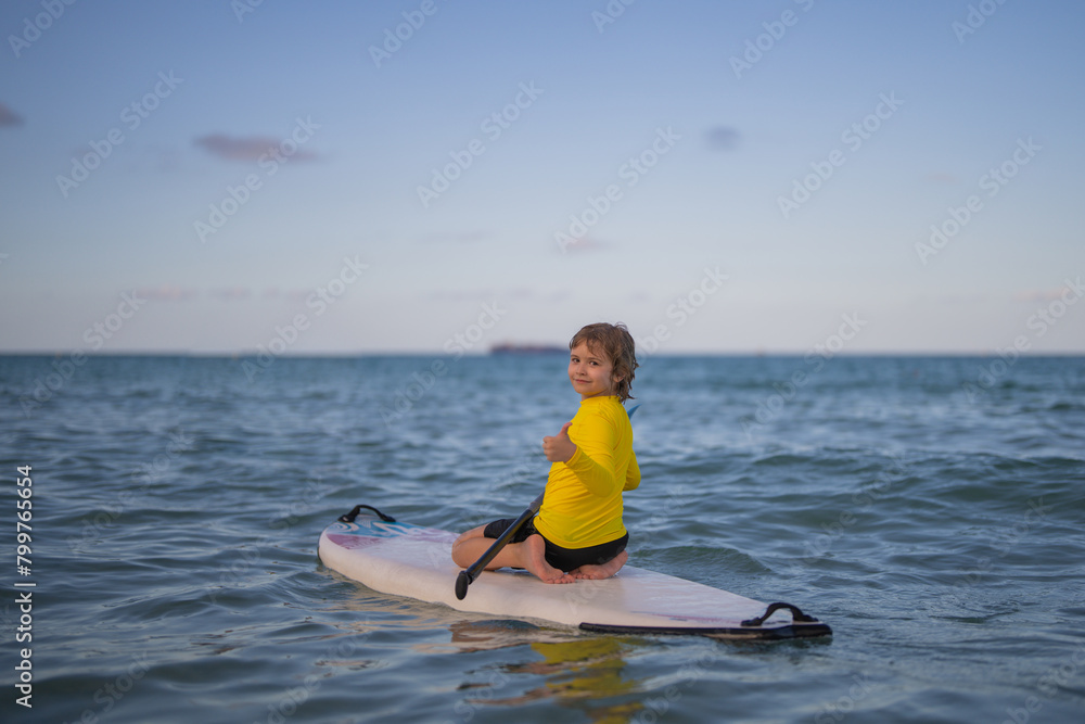 Obraz premium Kid Paddle boarder. Child boy paddling on paddleboard. Healthy summer lifestyle. Summer Water sport. SUP surfing tour in adventure summer beach vacation. Kid Boy swimming with paddle board.
