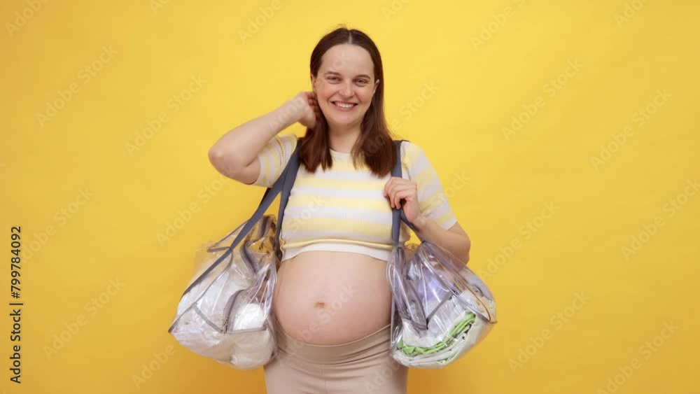 pretty pleased Caucasian pregnant woman with bare belly wearing casual top isolated over yellow background holding bags on shoulders smiling to camera preparing to hospital with happy face pretty pleased Caucasian pregnant woman with bare belly wearing casual top isolated over yellow background holding bags on shoulders smiling to camera preparing to hospital with happy face