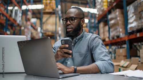 Strategic warehouse manager stays connected and productive, multitasking on laptop and phone.
