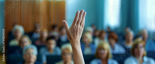 The hand of one person was raised in the audience while listening to an interview at a business conference or presentation. During the training class, people were sitting and raising their hands to as