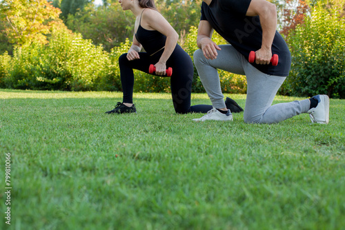 Detalle pareja de chico y chica haciendo pesas al aire libre. Mujer vestida de negro y hombre con camiseta negra y pantalón gris con pesas rojas. Chica en un parque haciendo deporte. Estilo de vida. C