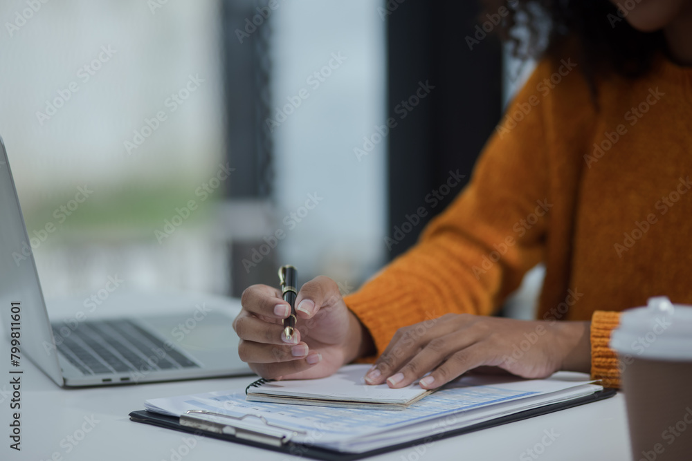 Fototapeta premium African American female working with laptop and calculator at desk in office.