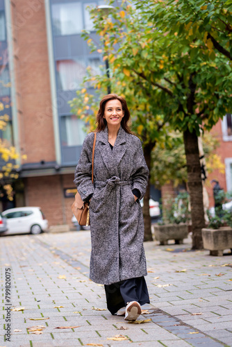 Brunette haired woman wearing tweed coat and walking outdoors in the city street on autumn day