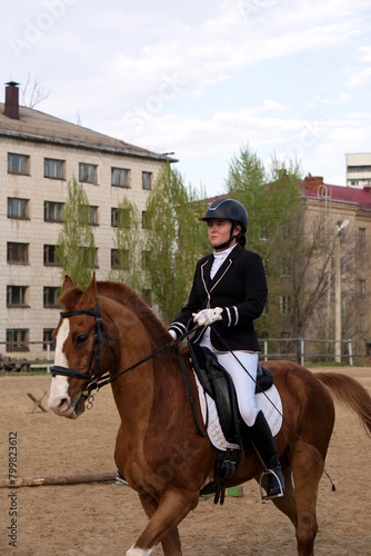 Rider on chestnut horse with urban backdrop © Vagengeim