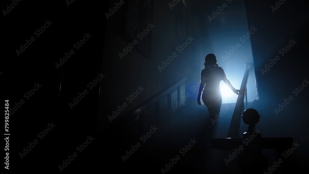Beauty and form. The silhouette of a beautiful, young woman against a dark background is climbing up the old stairs.