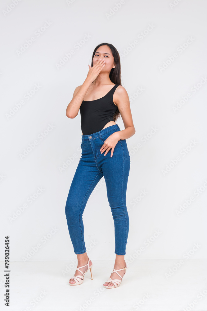 Front view of a young asian woman in a black bodysuit and jeans Isolated on a white background. Giggling covering her mouth. Whole body photo. Front view of a young asian woman in a black bodysuit and jeans Isolated on a white background. Giggling covering her mouth. Whole body photo.